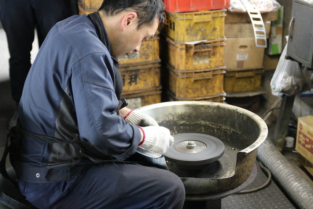 Koide-san honing a plane blade using a grinding wheel at Kakuri Works, focusing on precision in the sharpening process.