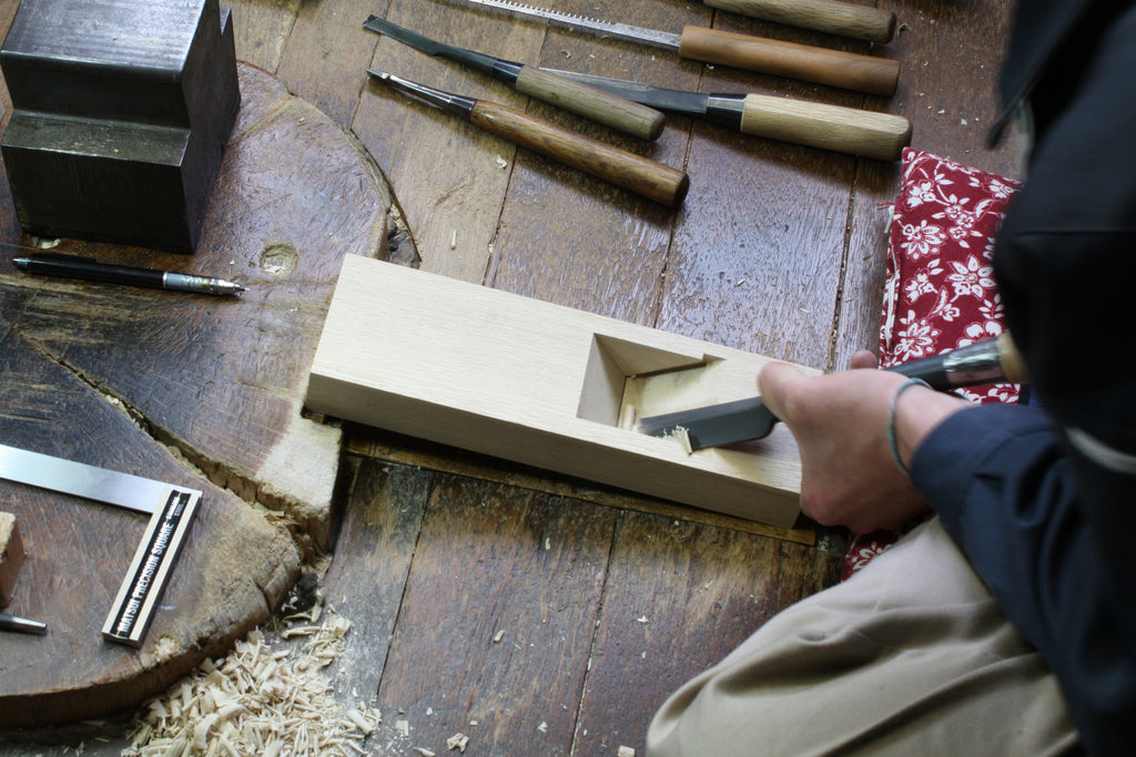 Craftsman carving wood with traditional Japanese tools, showcasing the precision and skill involved in woodworking.